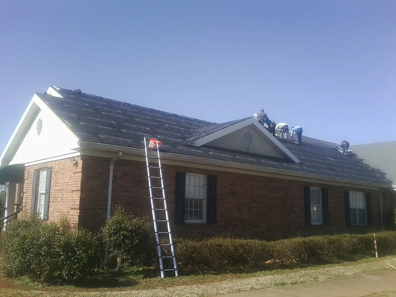 Crew tearing shingles off a brick ranch roof with a ladder set — Emergency Roof Repair work by our crew in Mellott