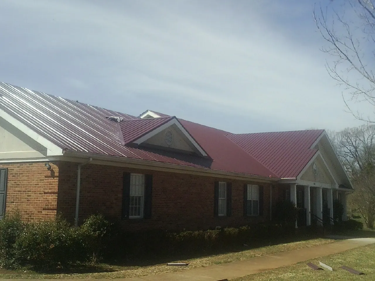 Red metal roof with gabled entries on a long brick building, from a Hail Damage Roof Repair job in Mellott