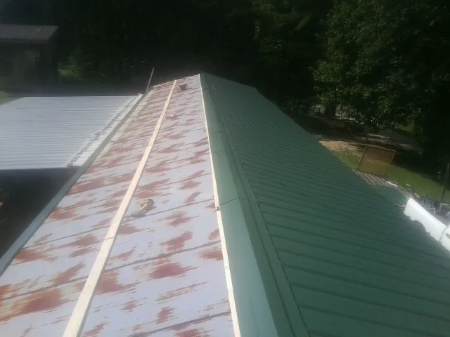 Old rusted panels beside newly installed green metal roofing — Wind Damage Roof Repair by Roofing Brothers in Mellott