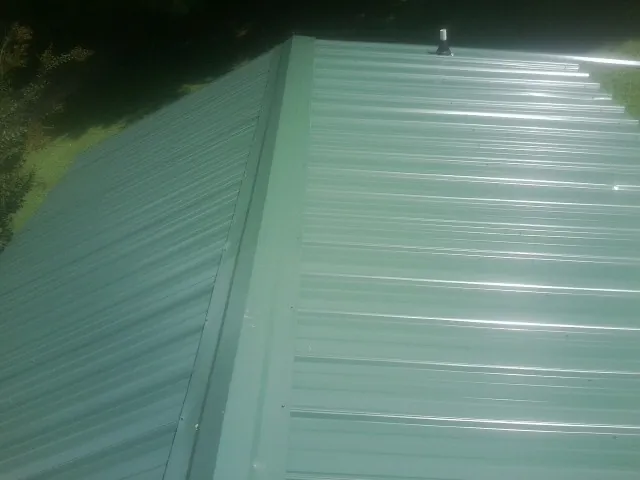 New green metal panels meeting at the ridge of a roof — Flat Roof Repair work by our crew in Mellott