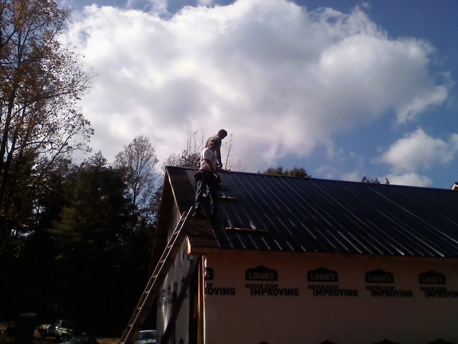 Roofer fastening dark metal panels high against a cloudy sky, from a Roof Inspection job in Mellott