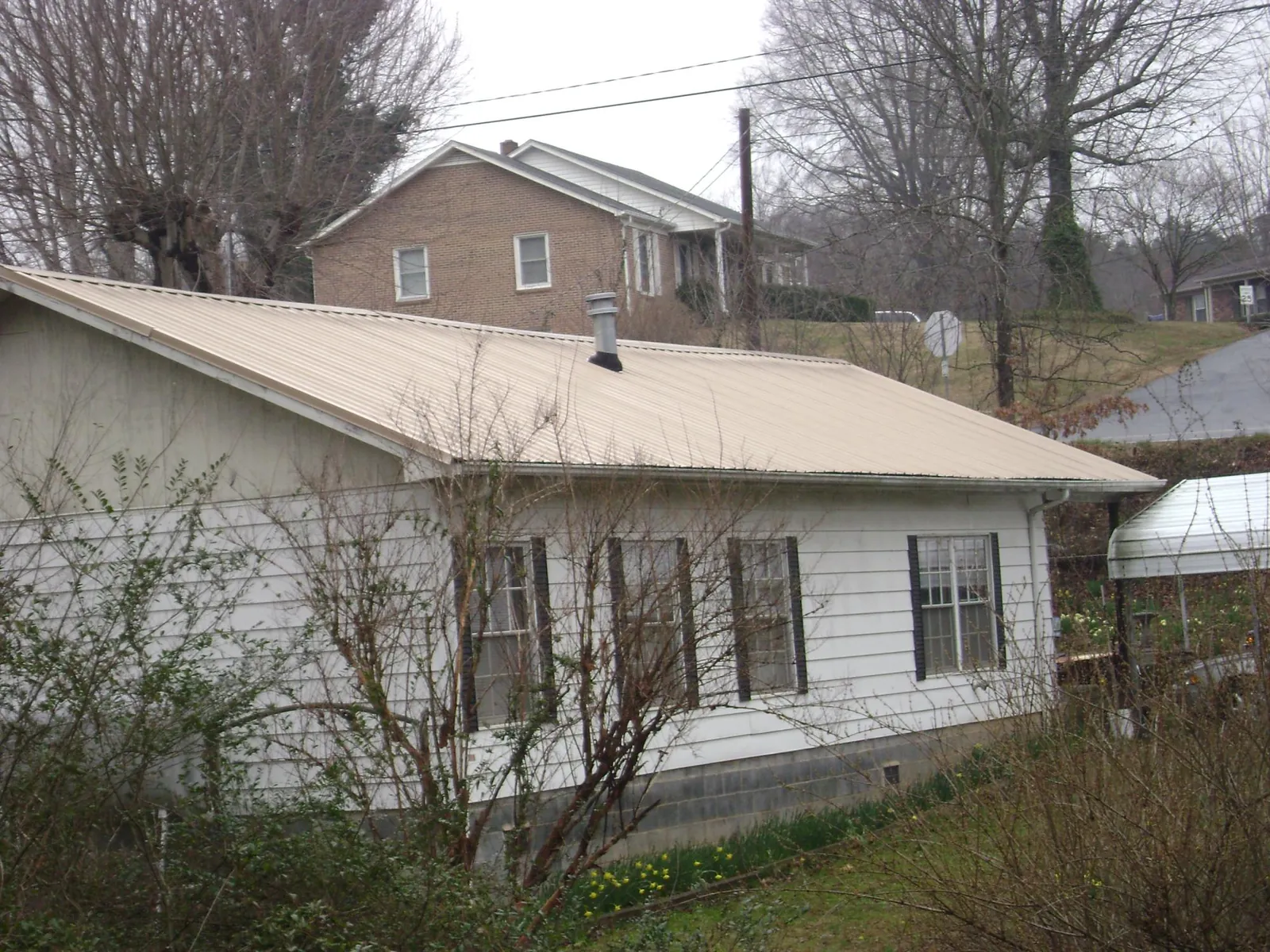 Tan metal roof on a white sided house set into a hillside — Commercial Roofing by Roofing Brothers in Mellott
